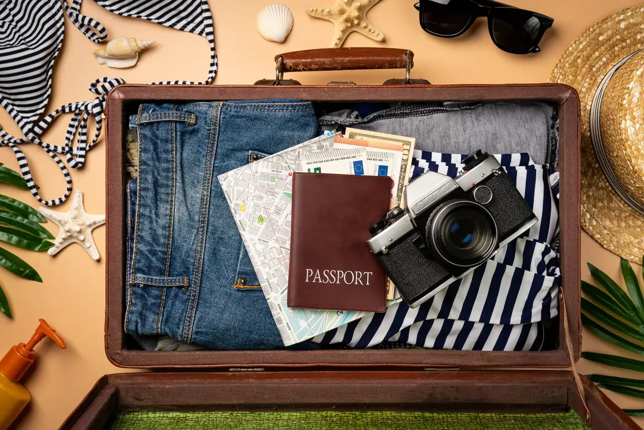 Geöffneter Reisekoffer mit Reisepass, Kamera und Kleidung von oben